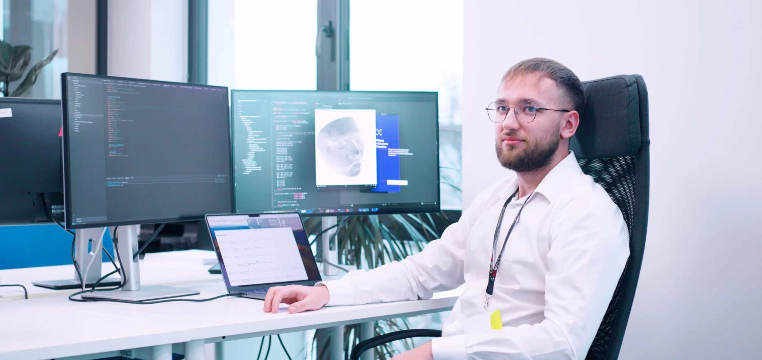 A software developer, seated at his desk in a modern office, is captured deep in thought. Sporting a white shirt and glasses, he works amidst a setup featuring two large monitors and a laptop, displaying lines of code and a detailed face scan. The well-lit workspace, accented by a leafy plant and large windows, reflects a contemporary and tech-savvy environment. A software developer, seated at his desk in a modern office, is captured deep in thought. Sporting a white shirt and glasses, he works amidst a setup featuring two large monitors and a laptop, displaying lines of code and a detailed face scan. The well-lit workspace, accented by a leafy plant and large windows, reflects a contemporary and tech-savvy environment.</p><p>
